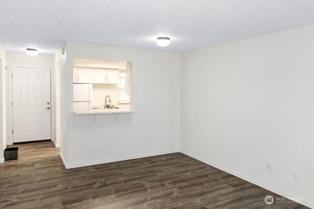 empty room featuring dark wood-style floors, a textured ceiling, baseboards, and a sink