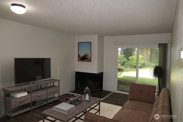 living area with a textured ceiling, wood finished floors, and a tiled fireplace