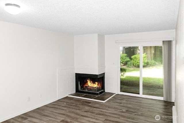 unfurnished living room with a multi sided fireplace, a textured ceiling, wood finished floors, and baseboards