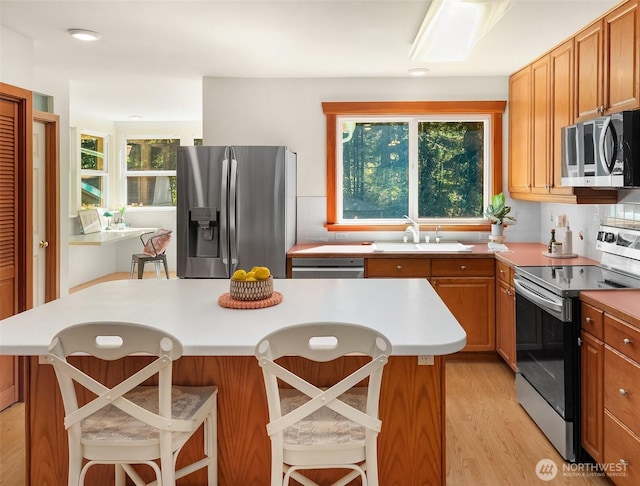 11607 SW Cove Rd, Vashon, WA 98070 - kitchen with stainless steel appliances, a sink, a kitchen island, light wood finished floors, and a breakfast bar area