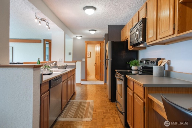 kitchen featuring appliances with stainless steel finishes, a textured ceiling, a sink, light countertops, and brown cabinets