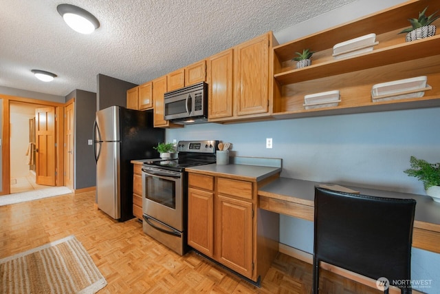 kitchen with appliances with stainless steel finishes, a textured ceiling, open shelves, baseboards, and a desk