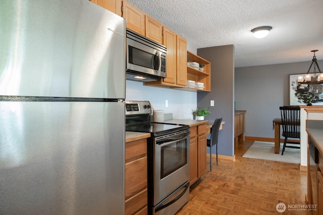 kitchen with appliances with stainless steel finishes, light brown cabinets, a textured ceiling, pendant lighting, and baseboards