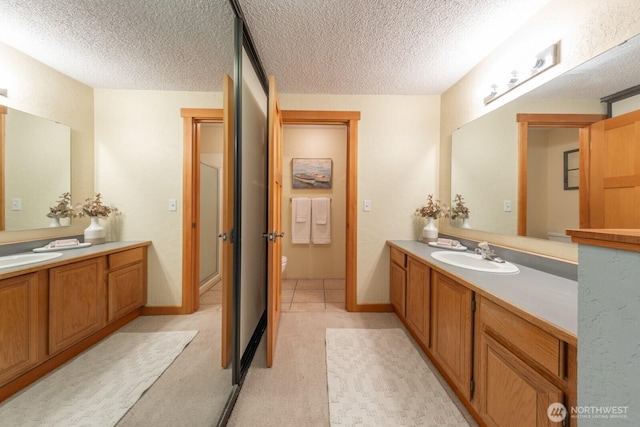 bathroom with a textured ceiling, two vanities, a shower stall, and toilet