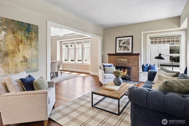living room featuring a brick fireplace, wood finished floors, and baseboards