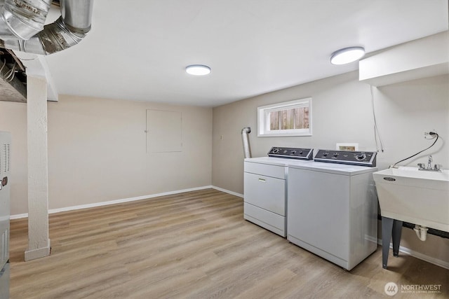 clothes washing area with washer and clothes dryer, light wood-style flooring, and baseboards