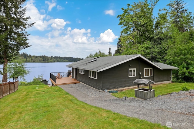 view of side of home with a deck with water view, a lawn, and a wooded view