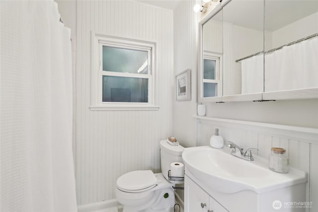 full bath featuring toilet, vanity, a decorative wall, curtained shower, and a wainscoted wall