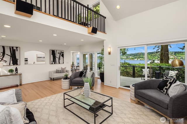 living area featuring wood finished floors, recessed lighting, high vaulted ceiling, baseboards, and a water view