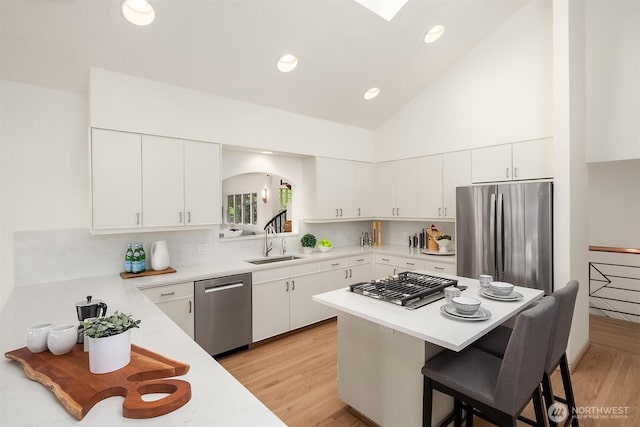 kitchen with appliances with stainless steel finishes, a sink, a kitchen bar, light countertops, and a kitchen island