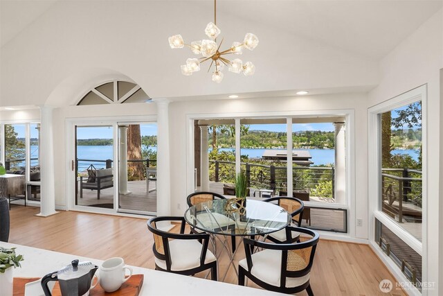 dining area featuring ornate columns, light wood-type flooring, a water view, high vaulted ceiling, and recessed lighting