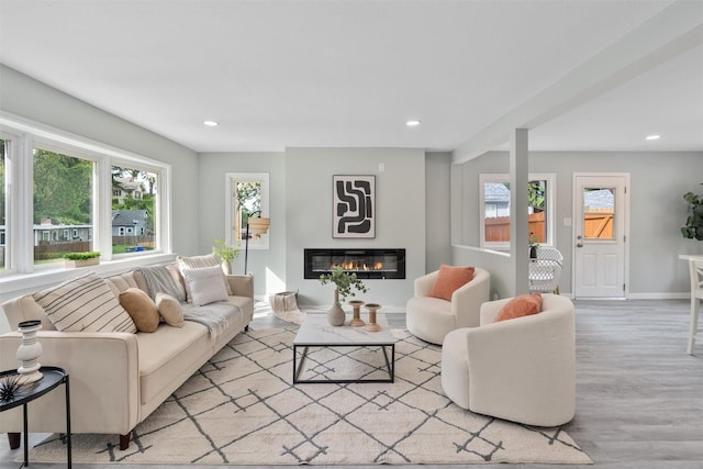 living area with wood finished floors, healthy amount of natural light, a glass covered fireplace, recessed lighting, and baseboards