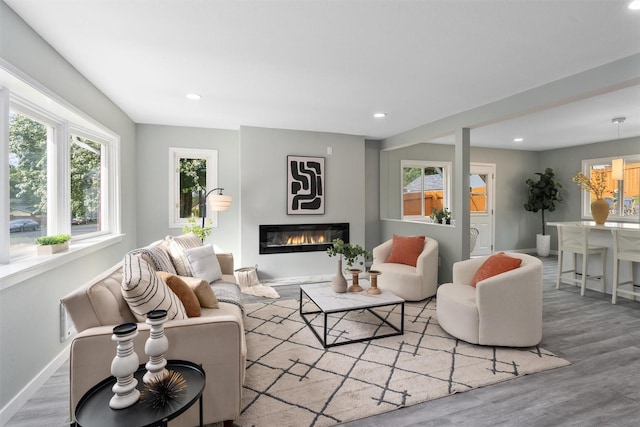 living room with recessed lighting, baseboards, plenty of natural light, wood finished floors, and a glass covered fireplace