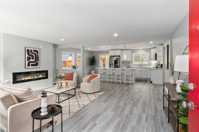living room with a glass covered fireplace, light wood-style flooring, and recessed lighting