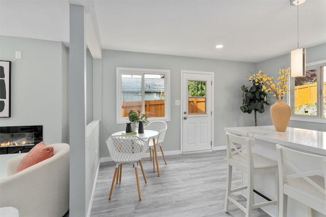 dining space with light wood-style floors, baseboards, recessed lighting, and a glass covered fireplace