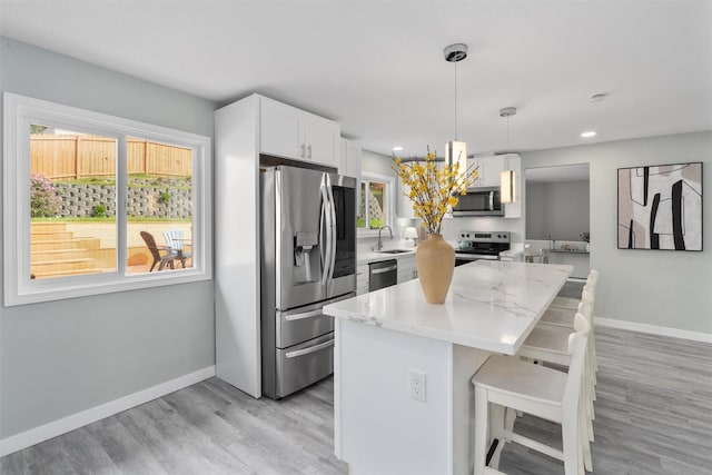 kitchen featuring appliances with stainless steel finishes, light wood-type flooring, white cabinets, a breakfast bar area, and a kitchen island