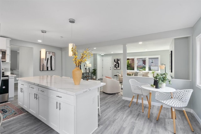 kitchen with light wood-style floors, recessed lighting, white cabinets, stainless steel microwave, and a kitchen island
