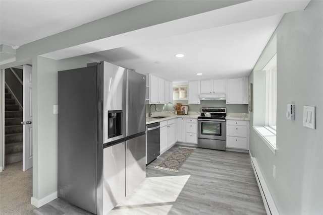 kitchen featuring appliances with stainless steel finishes, a sink, light countertops, baseboard heating, and white cabinetry