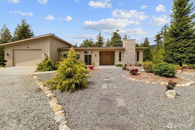 view of front facade with a garage, concrete driveway, a chimney, and board and batten siding