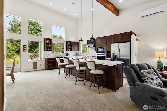 kitchen with a towering ceiling, stainless steel appliances, an AC wall unit, open floor plan, and light countertops