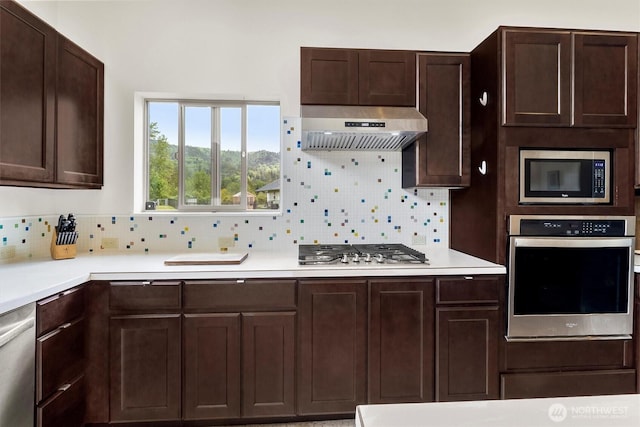 kitchen featuring stainless steel appliances, under cabinet range hood, decorative backsplash, light countertops, and dark brown cabinetry