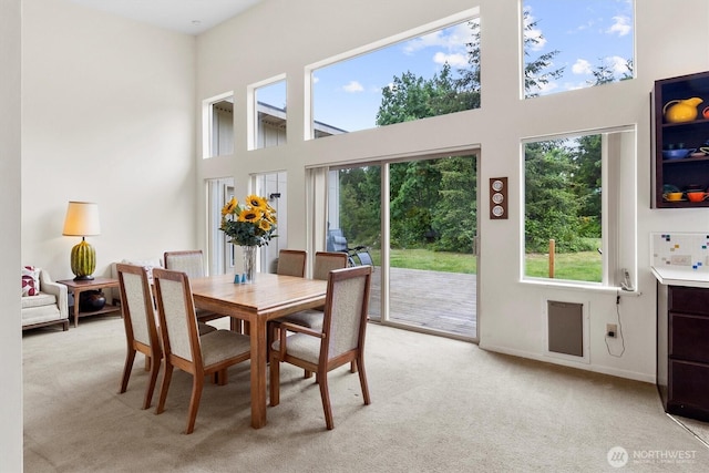 dining area with healthy amount of natural light, light colored carpet, and a towering ceiling