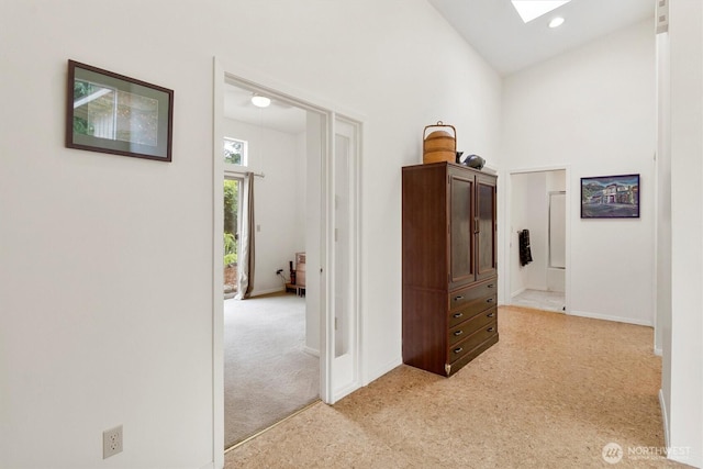 hall featuring light carpet, high vaulted ceiling, a skylight, and baseboards