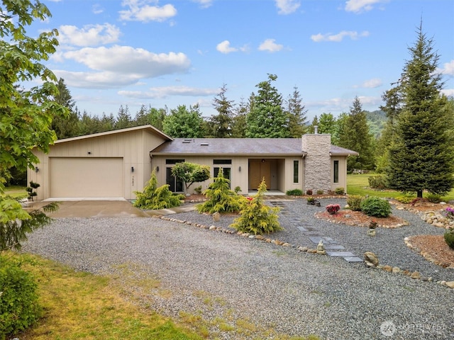 view of front facade with gravel driveway, a garage, and a chimney