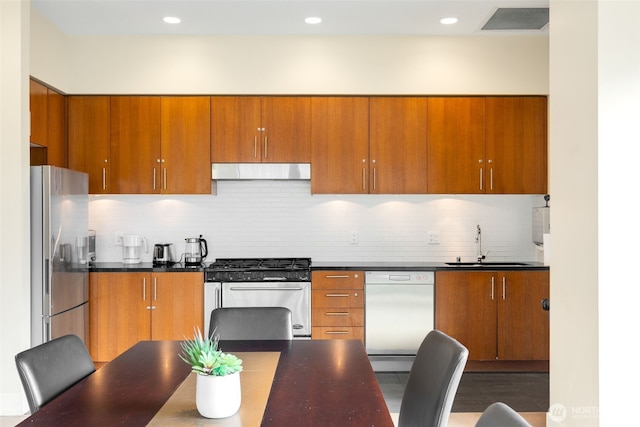 2721 1st Ave Unit 407, Seattle, WA 98121 - kitchen with appliances with stainless steel finishes, under cabinet range hood, a sink, brown cabinetry, and dark countertops