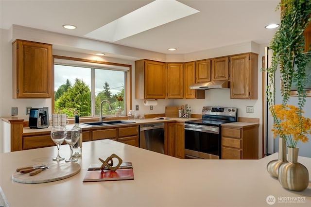 kitchen featuring appliances with stainless steel finishes, a sink, under cabinet range hood, light countertops, and a skylight