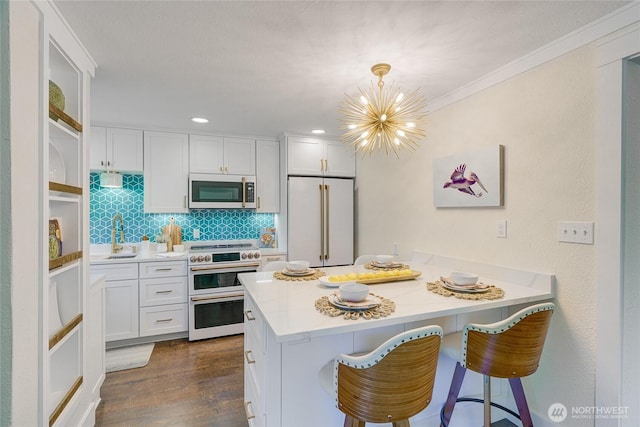 kitchen with high end appliances, a peninsula, a breakfast bar area, white cabinetry, and crown molding