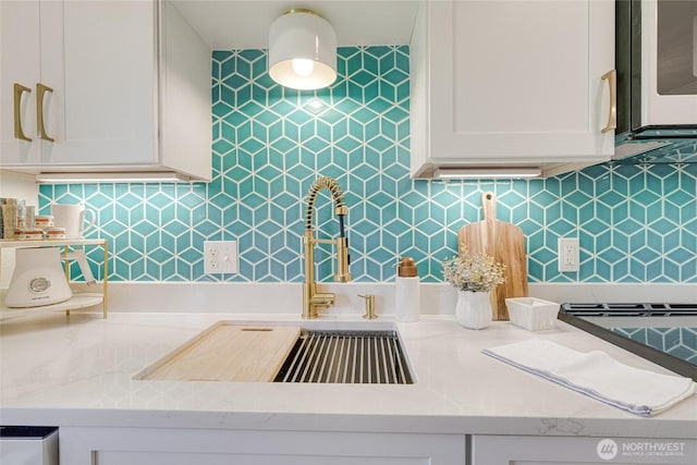 kitchen with white microwave, white cabinets, a sink, decorative backsplash, and light stone countertops