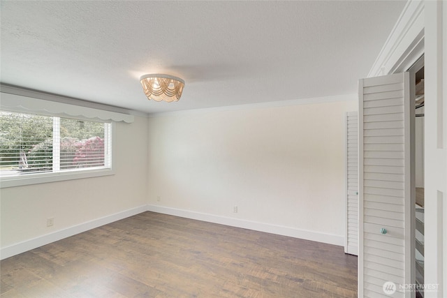 unfurnished bedroom with dark wood-type flooring, a chandelier, baseboards, crown molding, and a textured ceiling