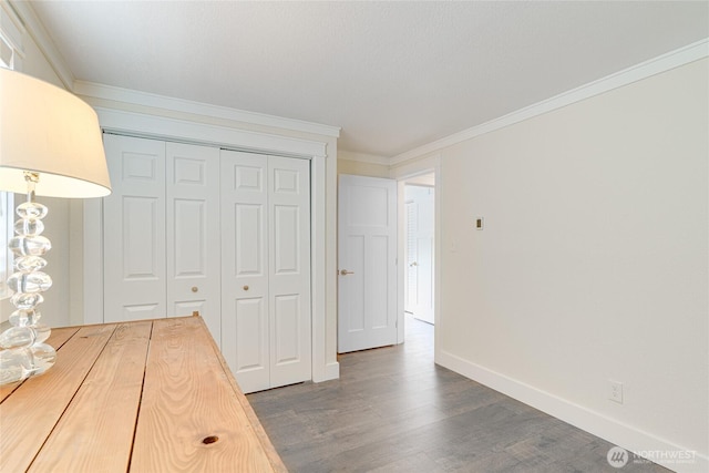 unfurnished bedroom with wood finished floors, baseboards, a closet, and crown molding