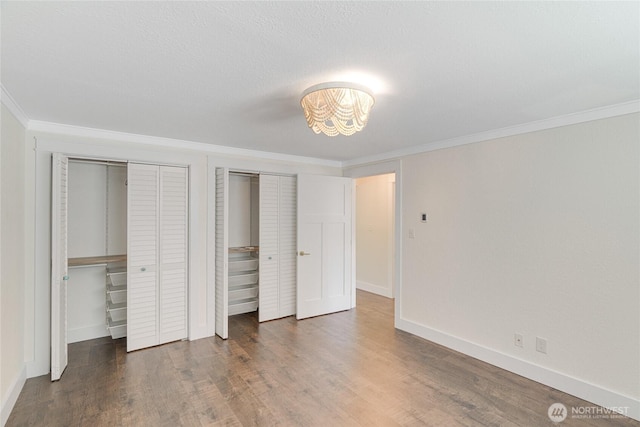 unfurnished bedroom with two closets, crown molding, wood finished floors, baseboards, and a chandelier