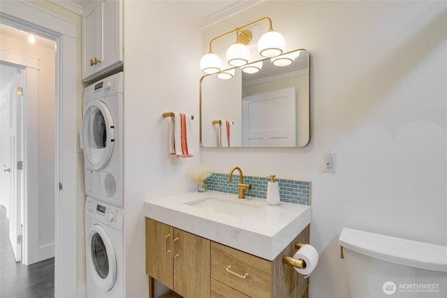 half bathroom featuring stacked washer and clothes dryer, tasteful backsplash, toilet, vanity, and crown molding