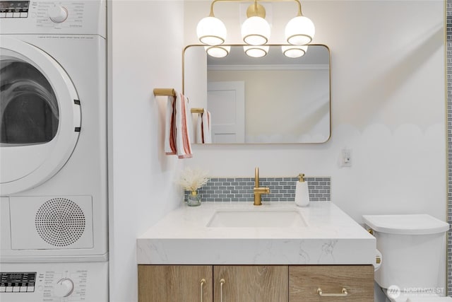 half bathroom featuring stacked washer / drying machine, backsplash, vanity, toilet, and crown molding