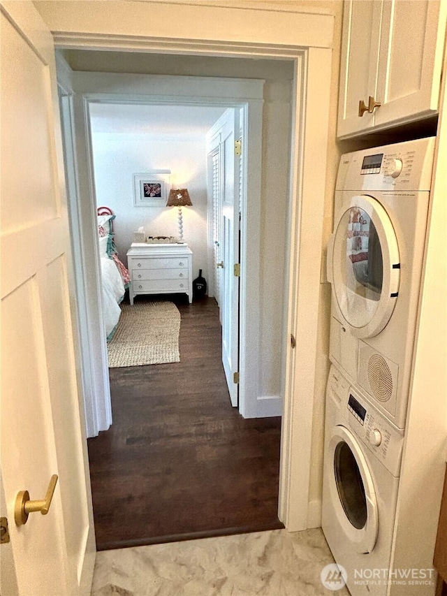 laundry room with stacked washer / drying machine, cabinet space, wood finished floors, and baseboards