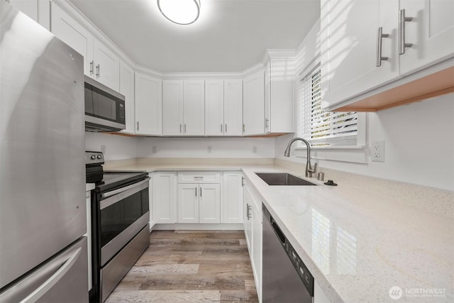 8322 Wabash Ave S, Seattle, WA 98118 - kitchen with appliances with stainless steel finishes, a sink, white cabinets, light wood-style flooring, and light stone countertops