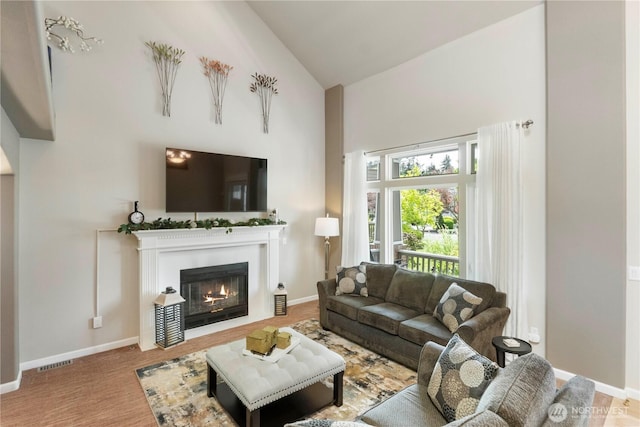 living area featuring high vaulted ceiling, a tiled fireplace, and baseboards
