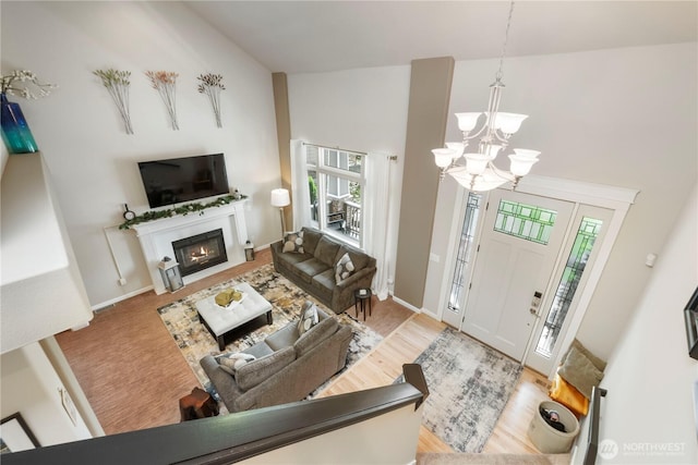 living room with plenty of natural light, a chandelier, a fireplace with flush hearth, wood finished floors, and high vaulted ceiling