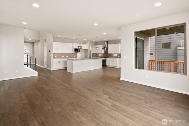 unfurnished living room featuring dark wood finished floors, recessed lighting, baseboards, stairway, and a sink