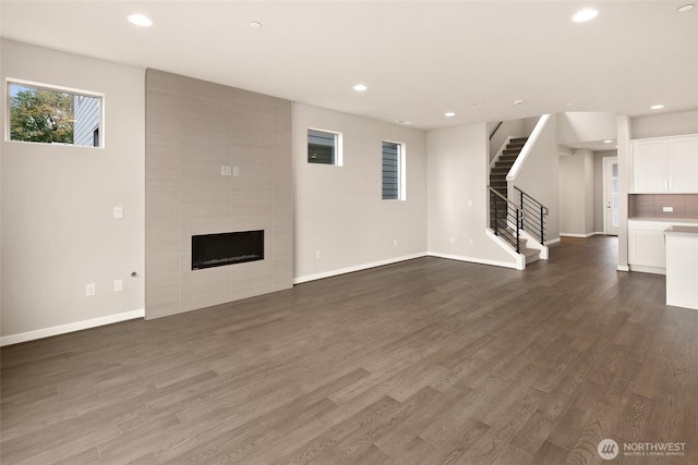 unfurnished living room with stairs, dark wood-type flooring, a tile fireplace, recessed lighting, and baseboards