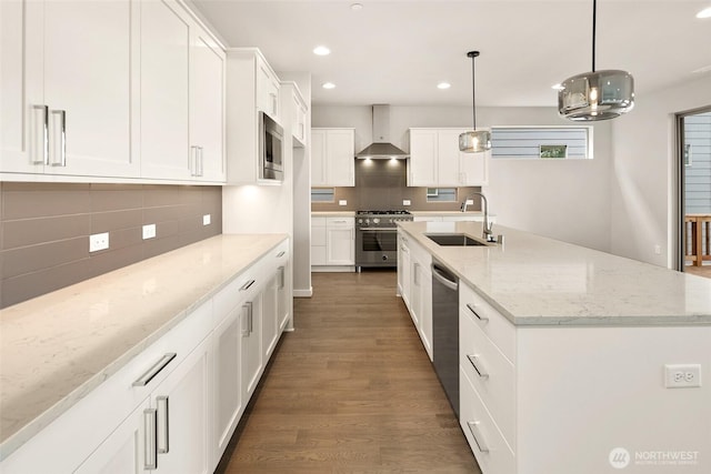 kitchen with a sink, appliances with stainless steel finishes, wall chimney range hood, recessed lighting, and white cabinetry