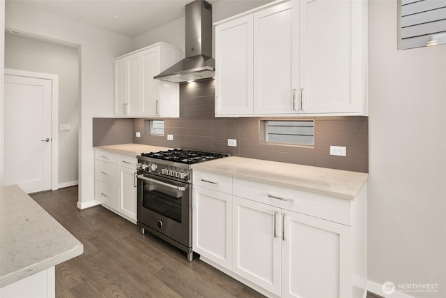 kitchen featuring high end stainless steel range oven, wall chimney range hood, dark wood-type flooring, backsplash, and white cabinetry