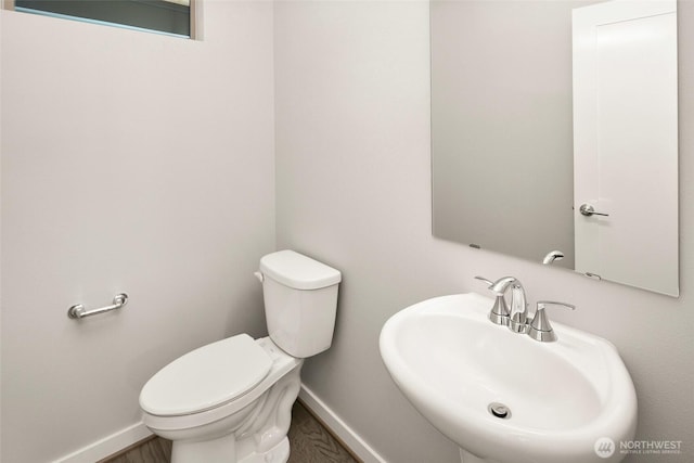 half bathroom with a sink, baseboards, and toilet