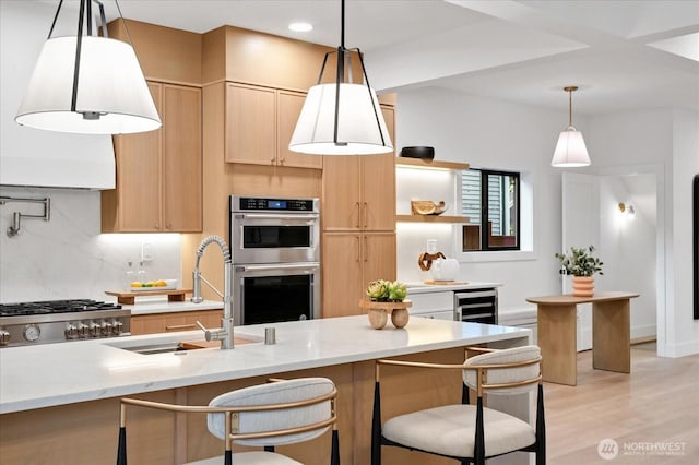 kitchen featuring stainless steel double oven, a sink, light brown cabinetry, tasteful backsplash, and light wood finished floors