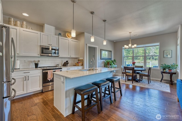 kitchen featuring stainless steel appliances, a sink, dark wood finished floors, decorative backsplash, and a chandelier