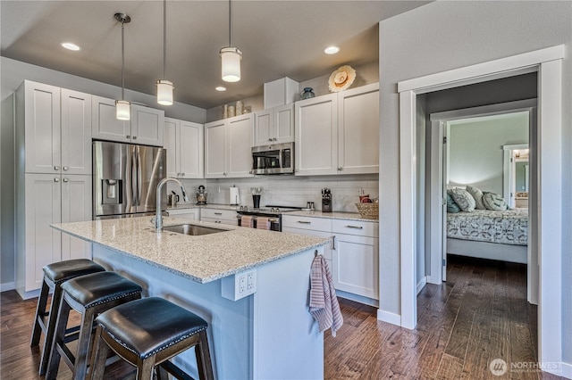 kitchen featuring appliances with stainless steel finishes, a sink, dark wood finished floors, a breakfast bar area, and light stone countertops