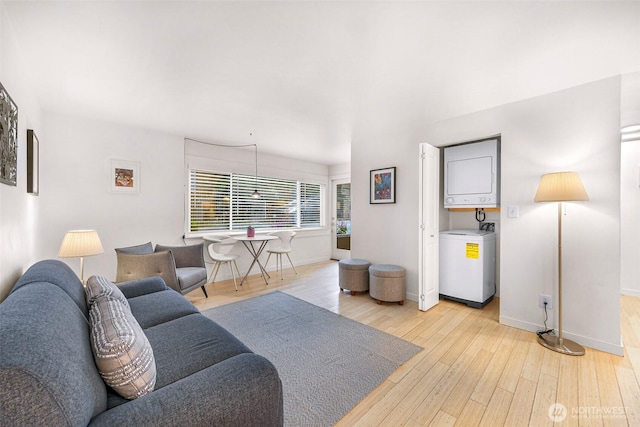 living room featuring estacked washer and dryer, light wood finished floors, and baseboards
